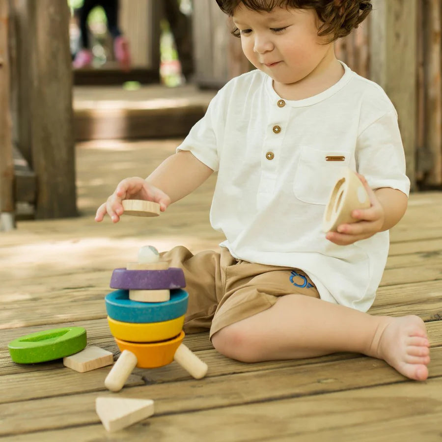 Child sitting on a wooden porch playing with stacking rocket