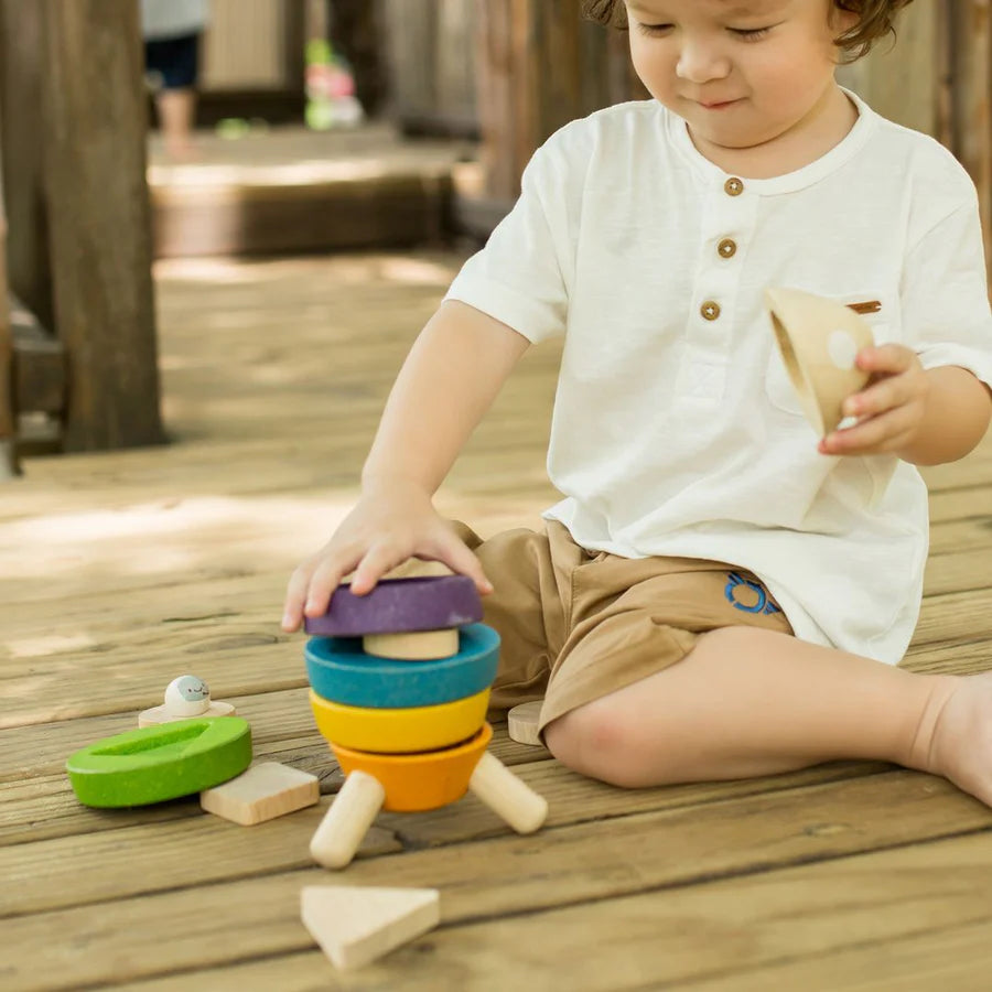 Child sitting on a wooden porch playing with stacking rocket