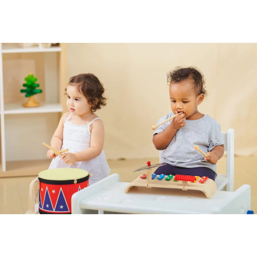 a child playing the drum next to a child playing with musical set