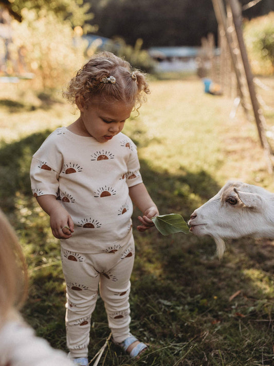 child feeding a goat wearing organic sun outfit by Ziwi Baby