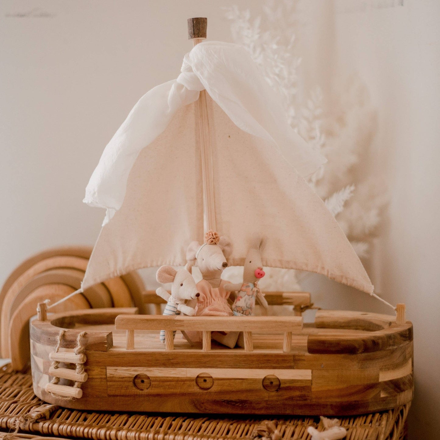 Wooden toy boat with a sail and small figurines on a textured surface.