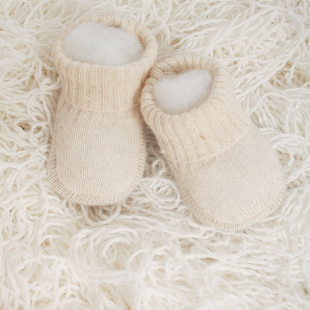 Newborn baby in a beige outfit lying in a wicker basket with soft textures and plants.