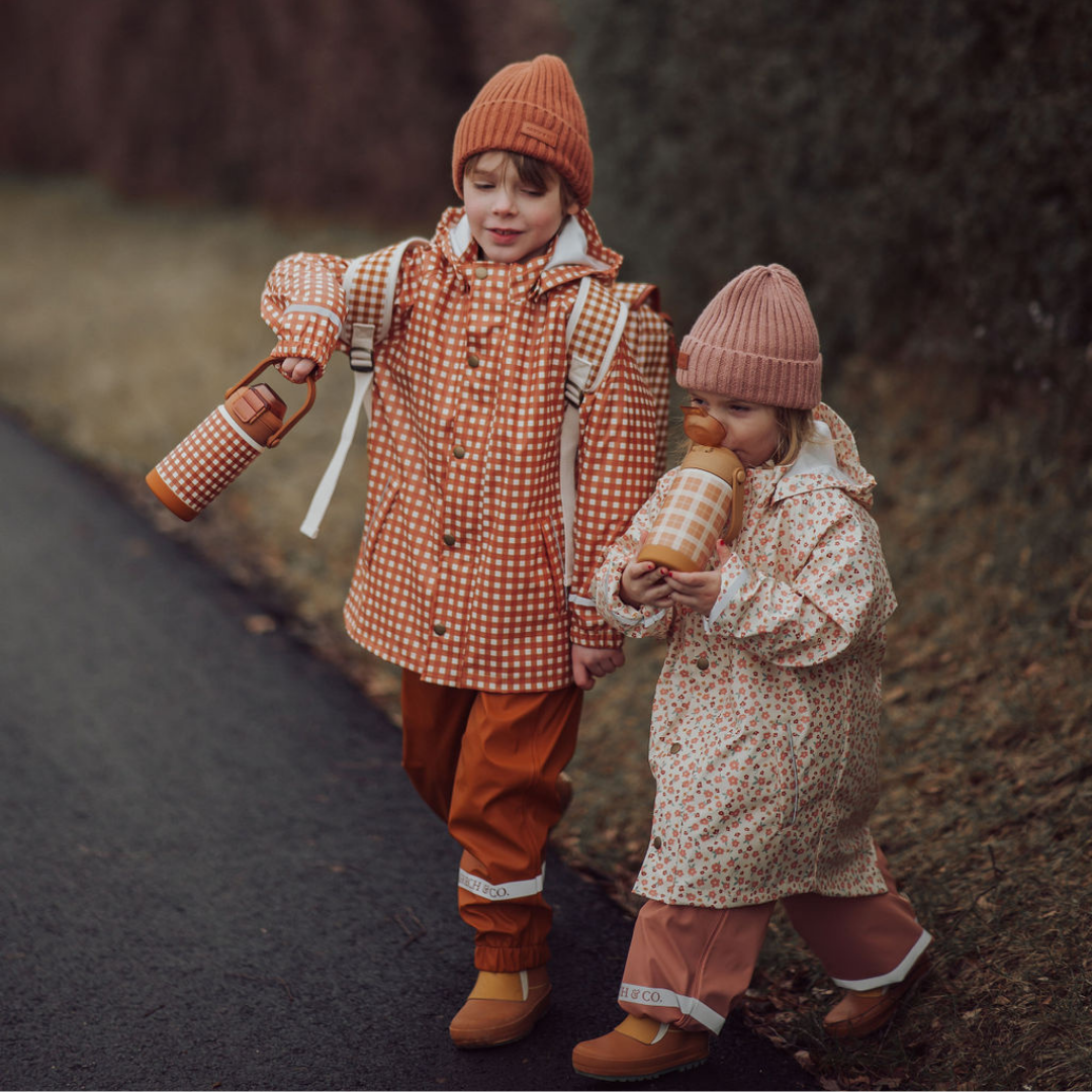 Two children in autumn-themed outfits standing on a path.