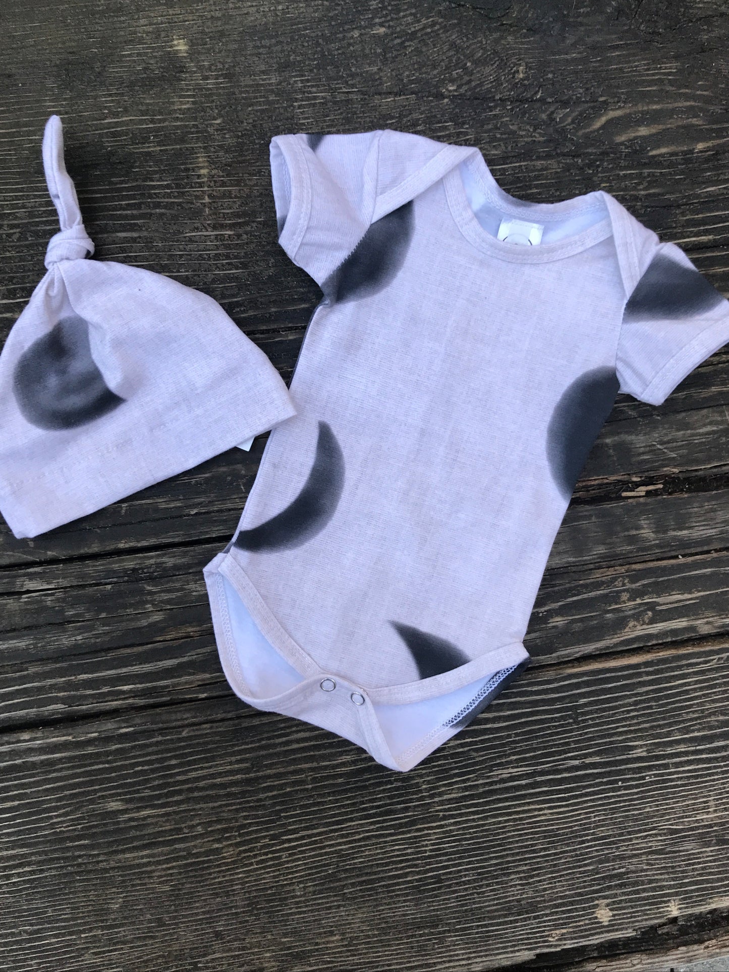 Short sleeve moon phase onesie with hat on a wood bench