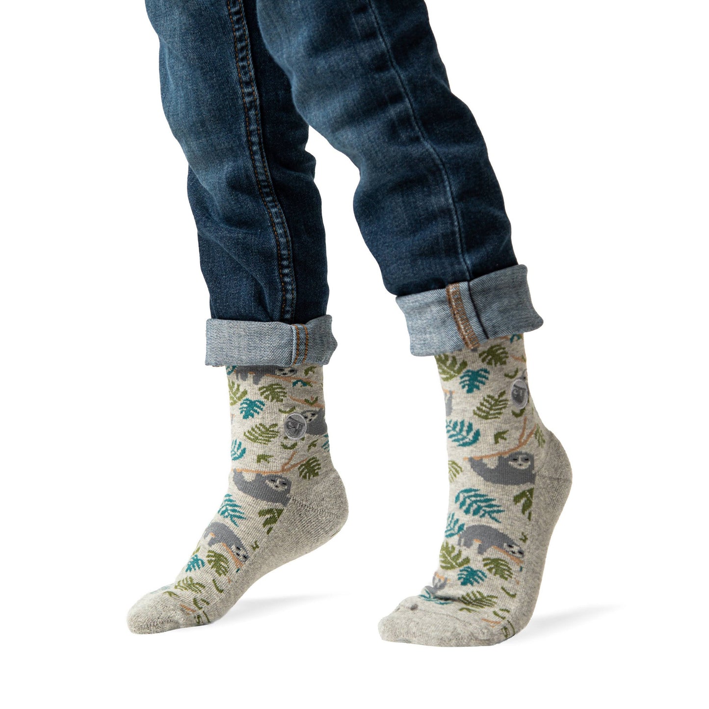 Person wearing patterned socks with sloths and leaves, paired with rolled-up jeans on a white background.