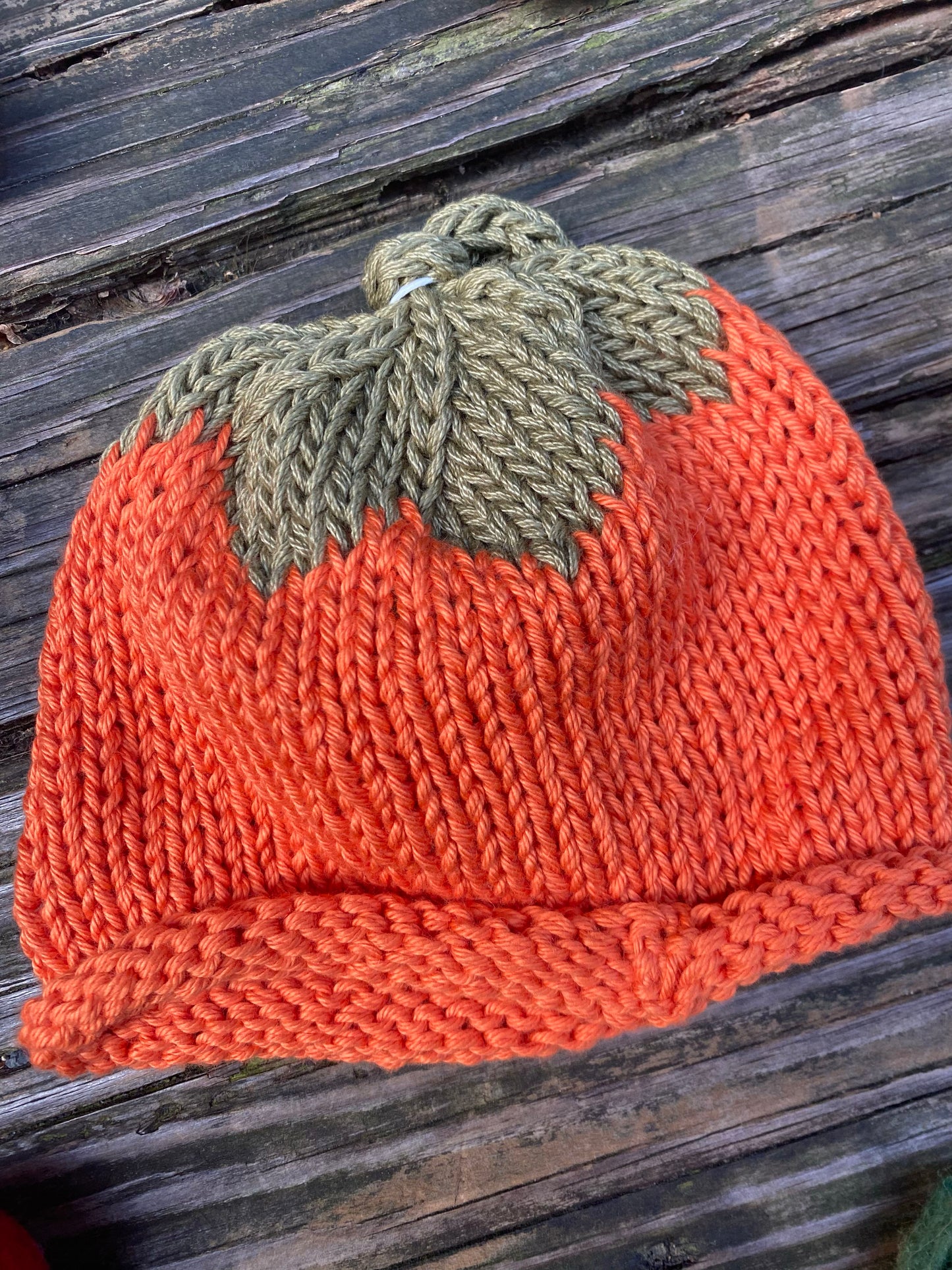 Knitted pumpkin hat with a green leaf on a wooden surface