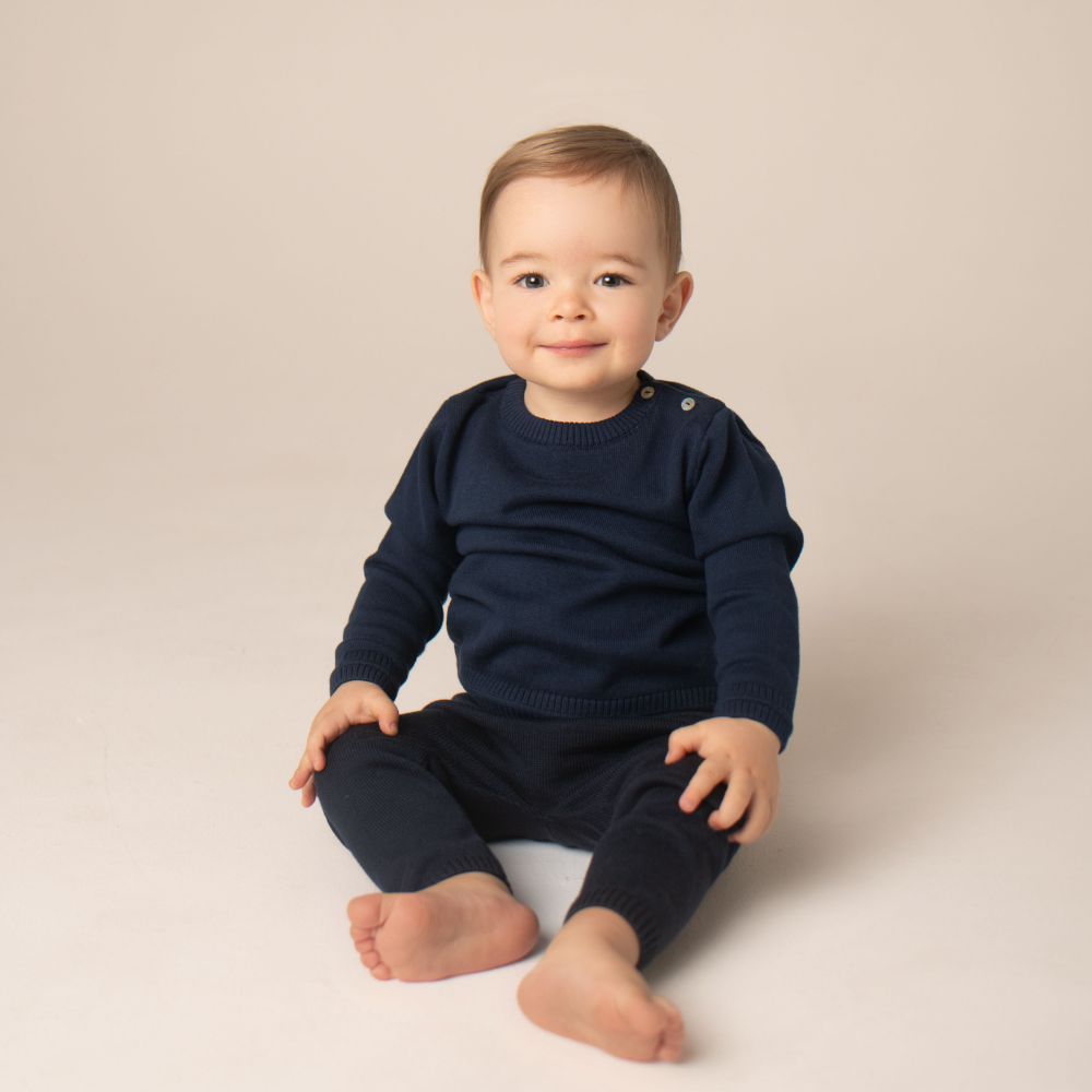 Baby wearing a navy blue outfit sitting on a beige background
