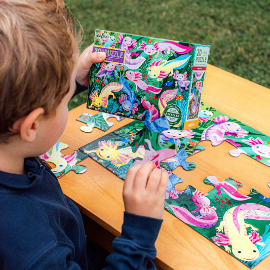 child wearing a blue sweater making Axolotl 20-Piece Puzzle on a wooden table outside