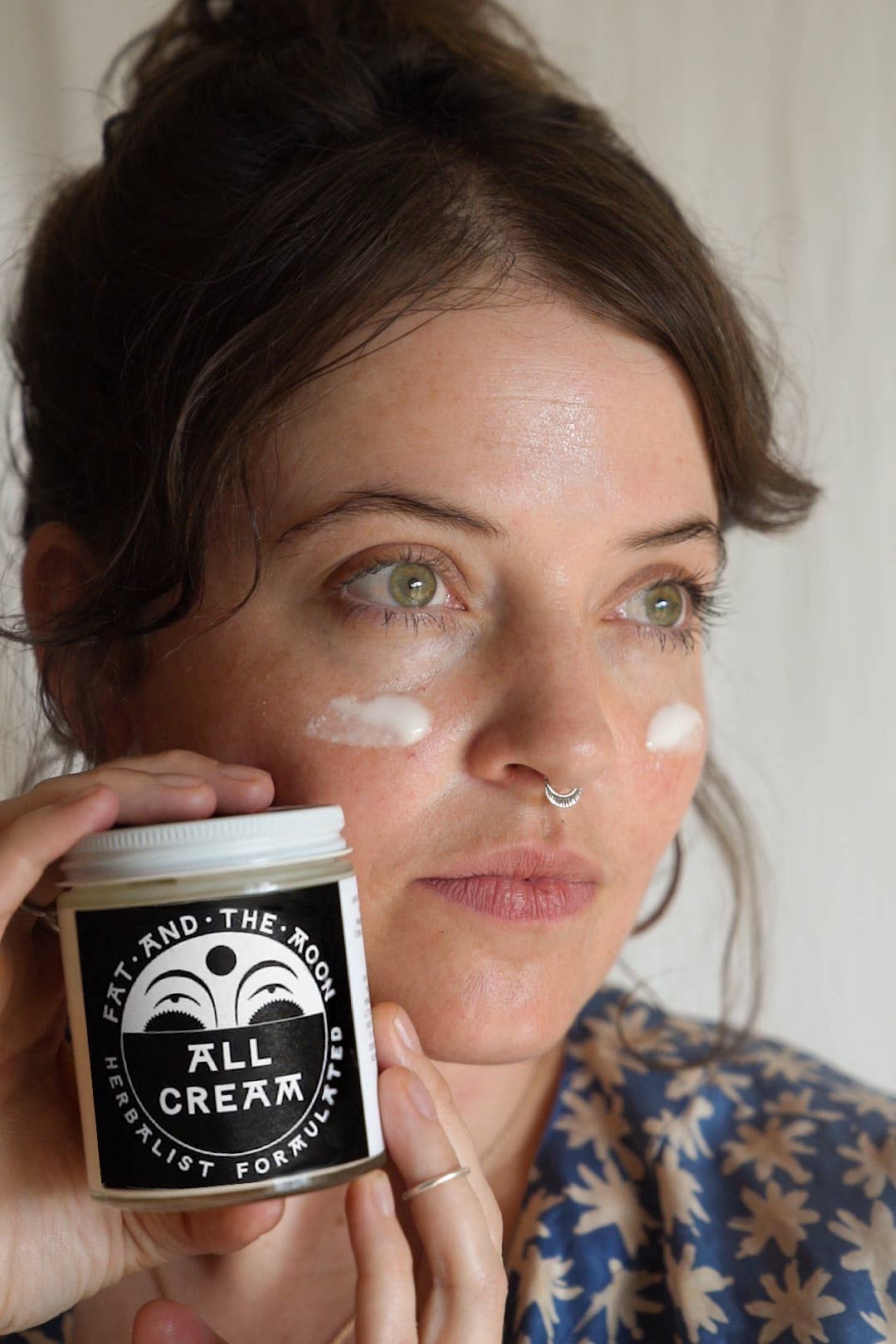 Person applying cream to her face with a jar labeled 'All Cream' in front of her.