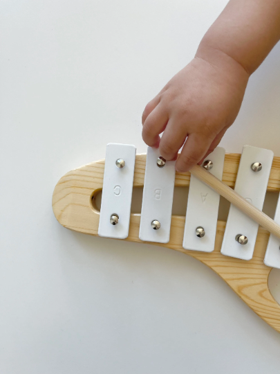Child's hand playing a small wooden xylophone on a white background