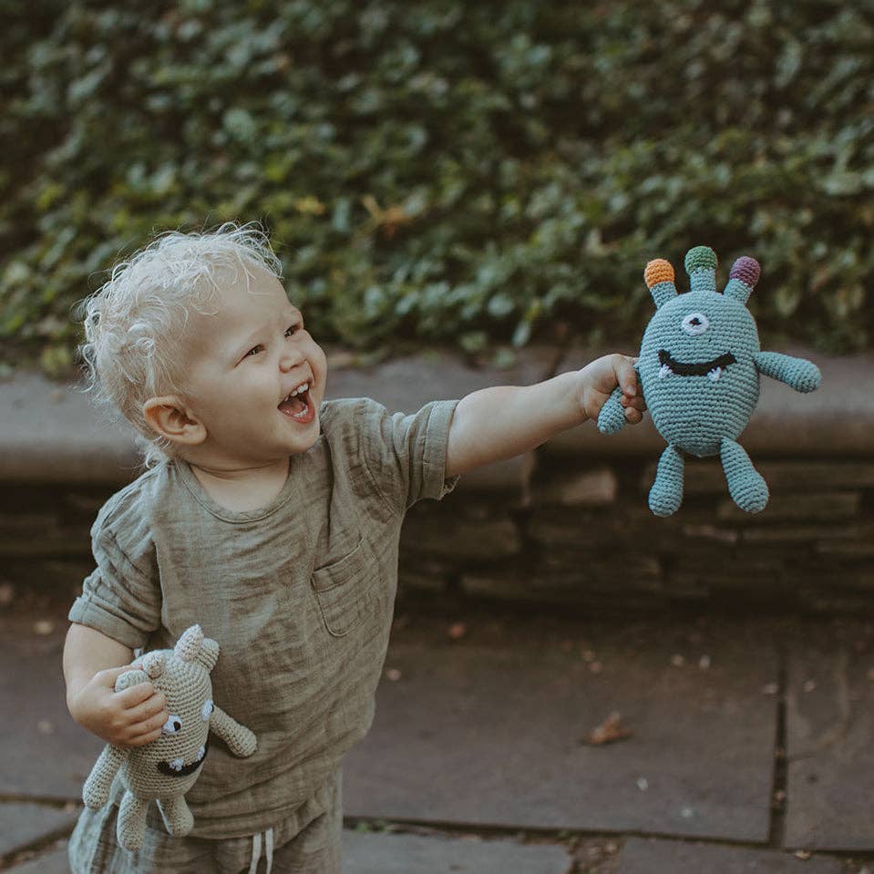 Child holding a knitted toy with a happy expression outdoors.