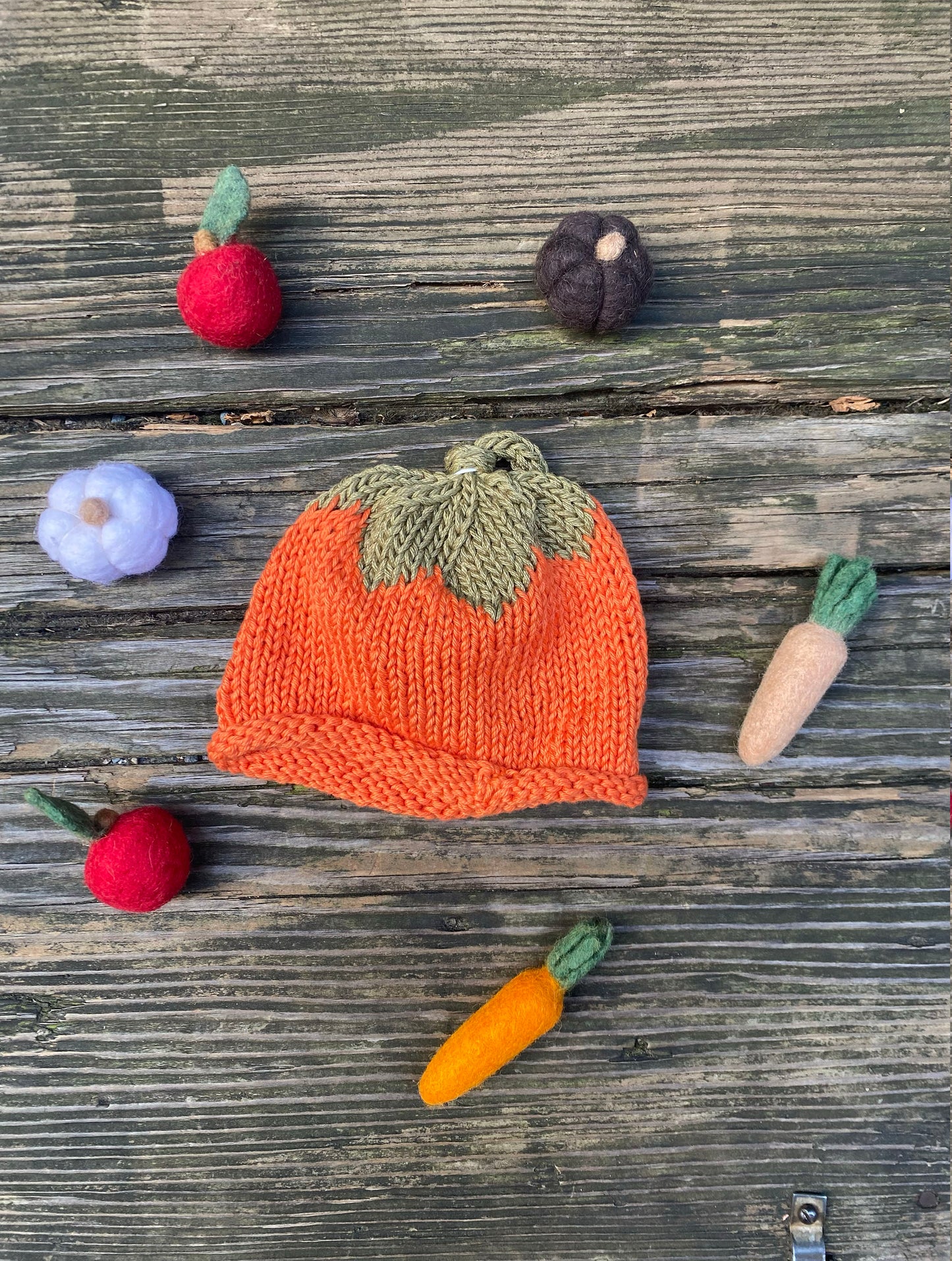 Knitted pumpkin hat with small vegetables on a wooden surface
