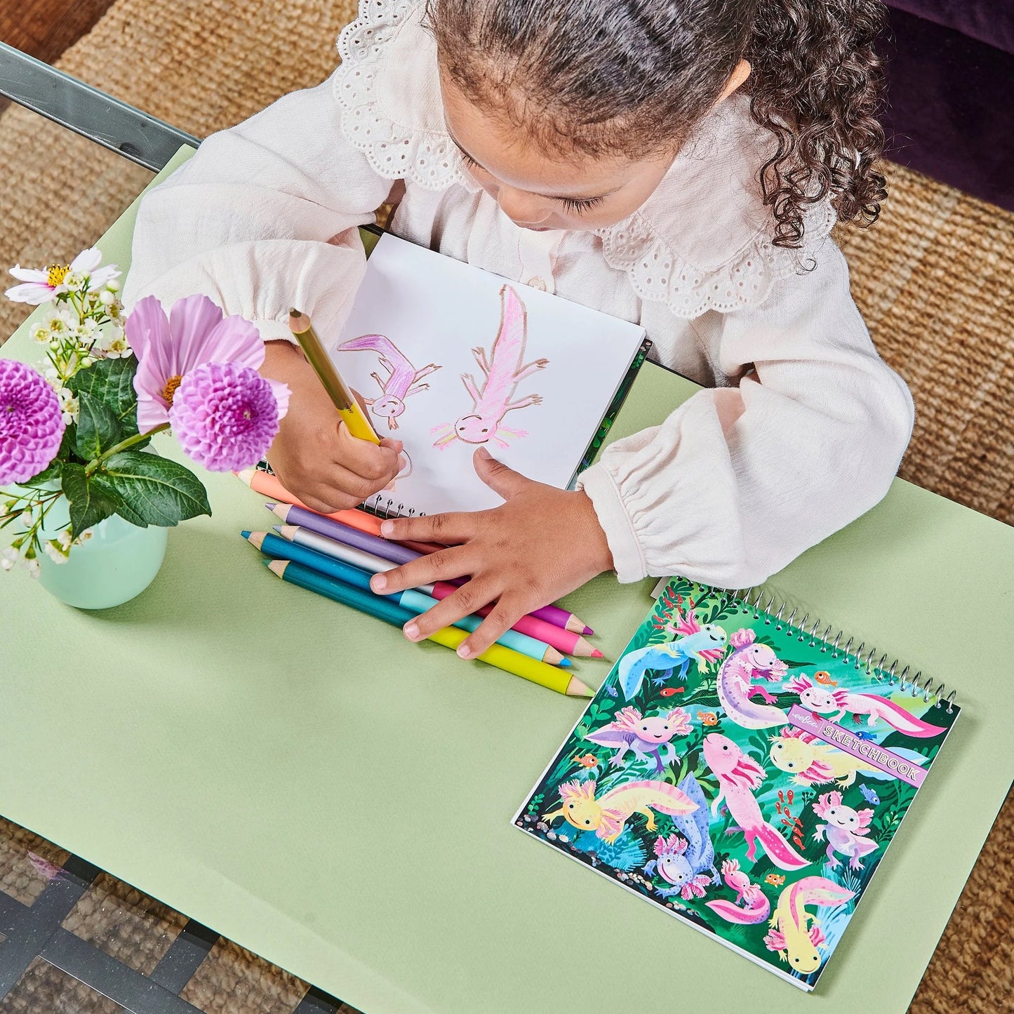 child sitting at a table drawing on an Axolotl square sketchbook