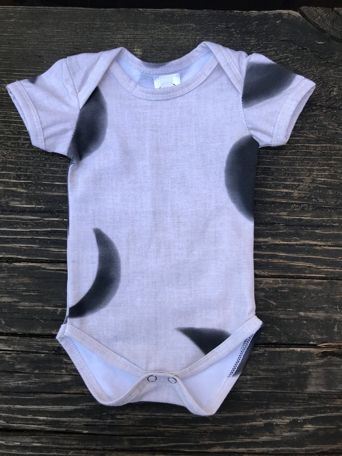 Short sleeve moon phase onesie on a wood bench