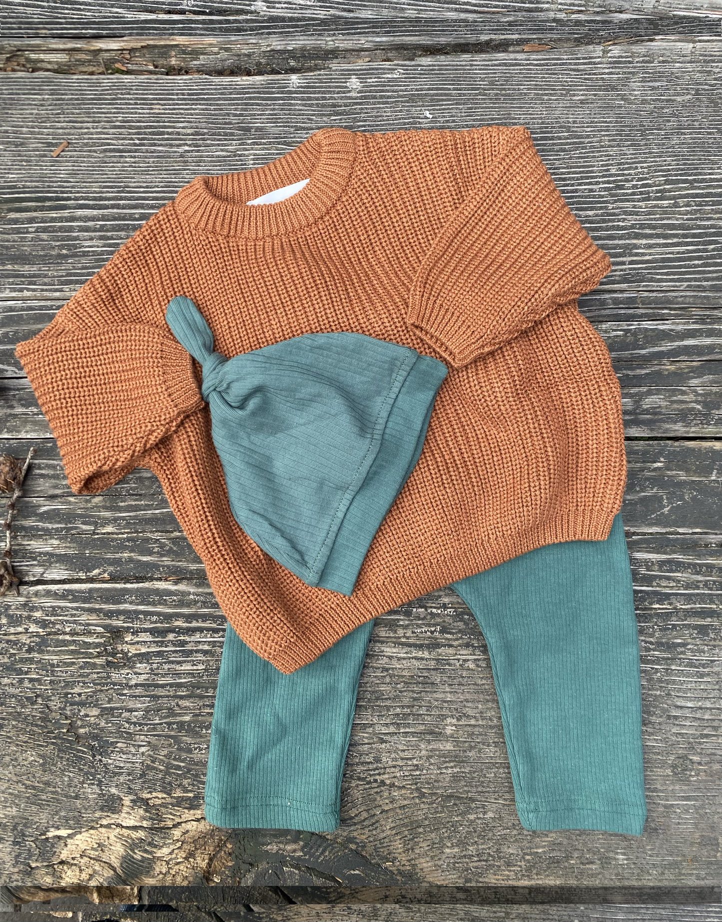 Children's outfit with clay sweater, green pants, and hat on a wooden surface