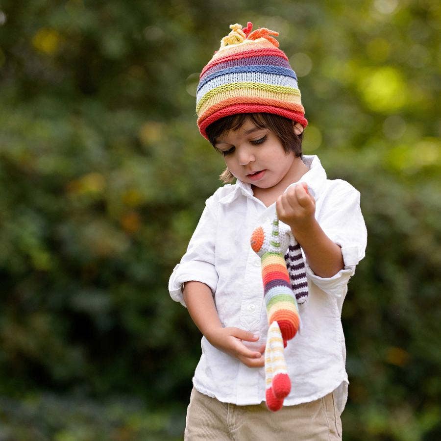 Child wearing a colorful striped hat and holding a matching scarf outdoors.
