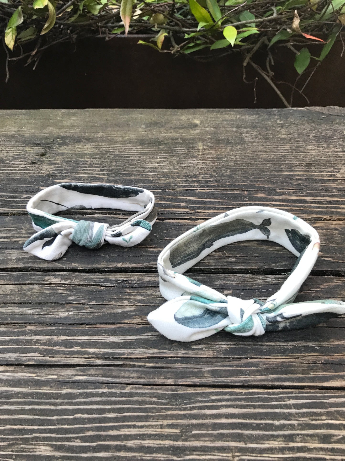Two Whale Song Baby Head Wraps on a wood bench