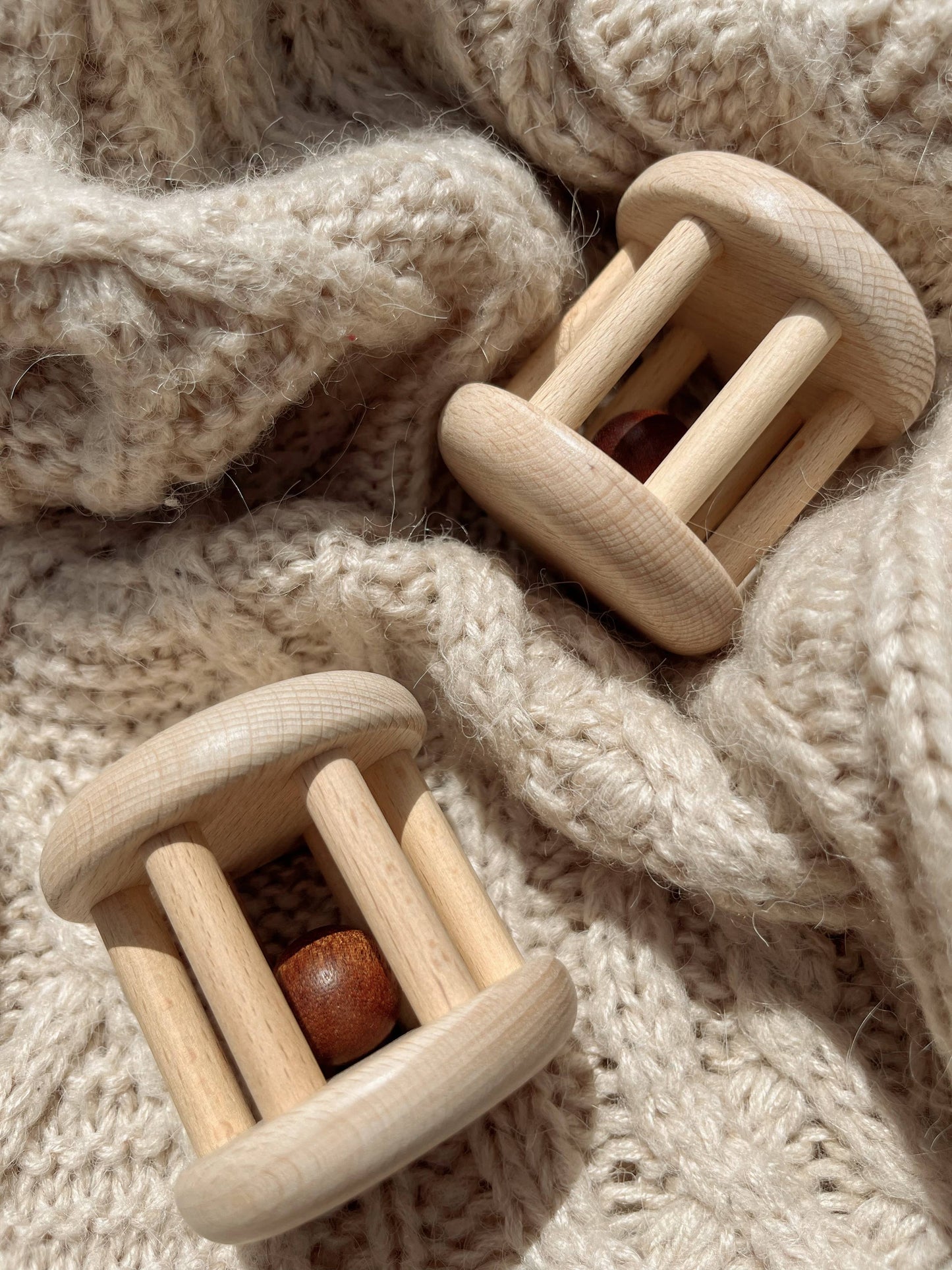Two wooden baby rattles on a soft, textured fabric background