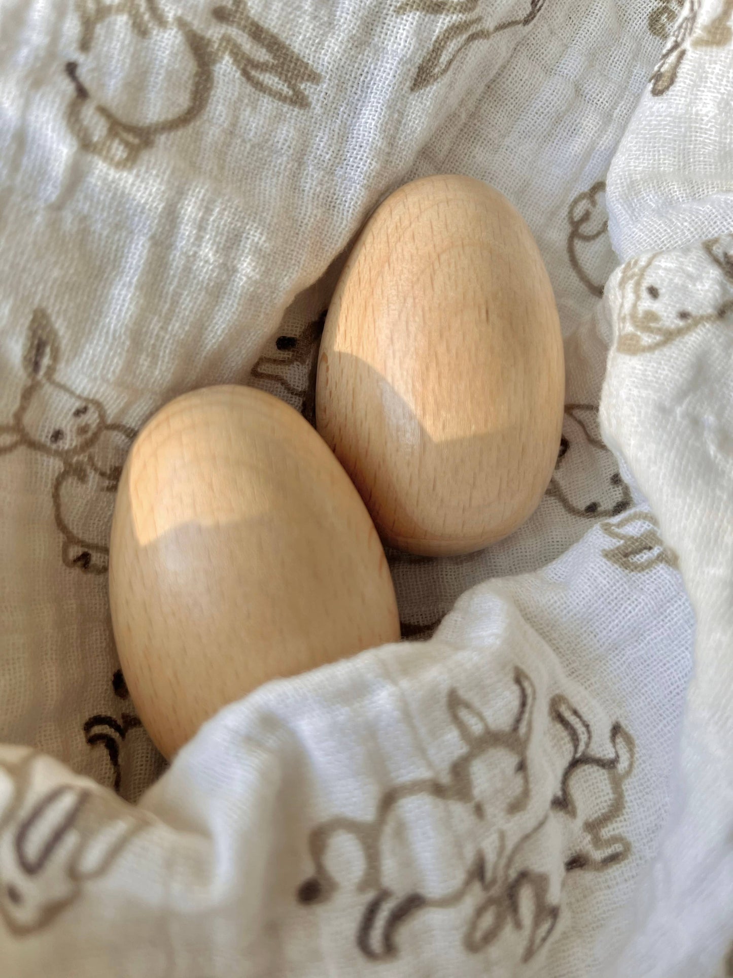 Two wooden egg shakers on a baby blanket with rabbit patterns