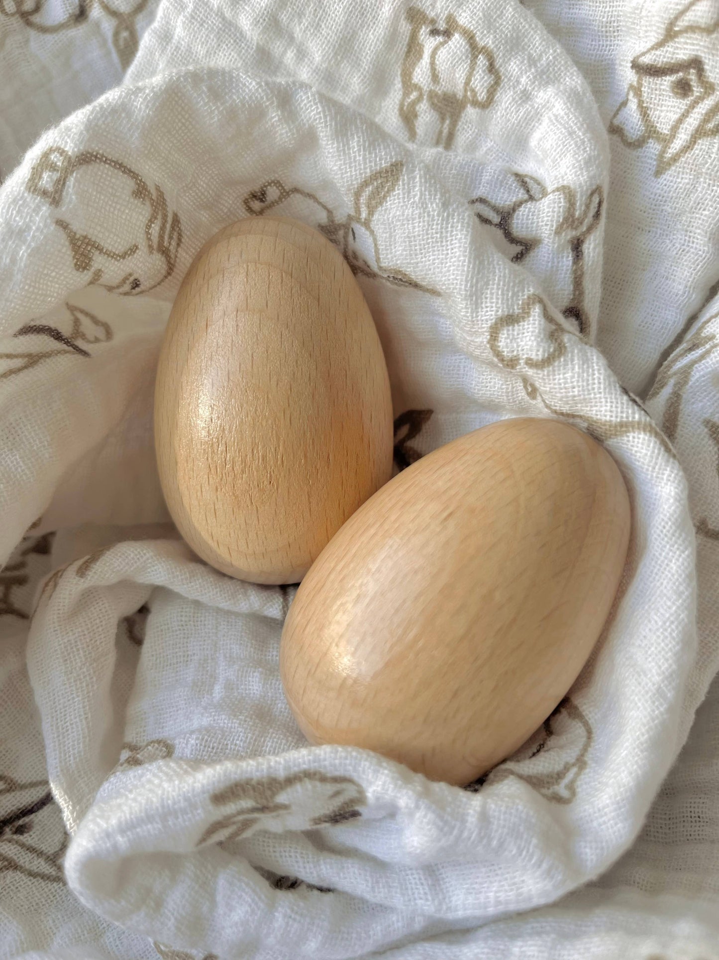 Two wooden egg shakers on a white baby blanket with animal prints