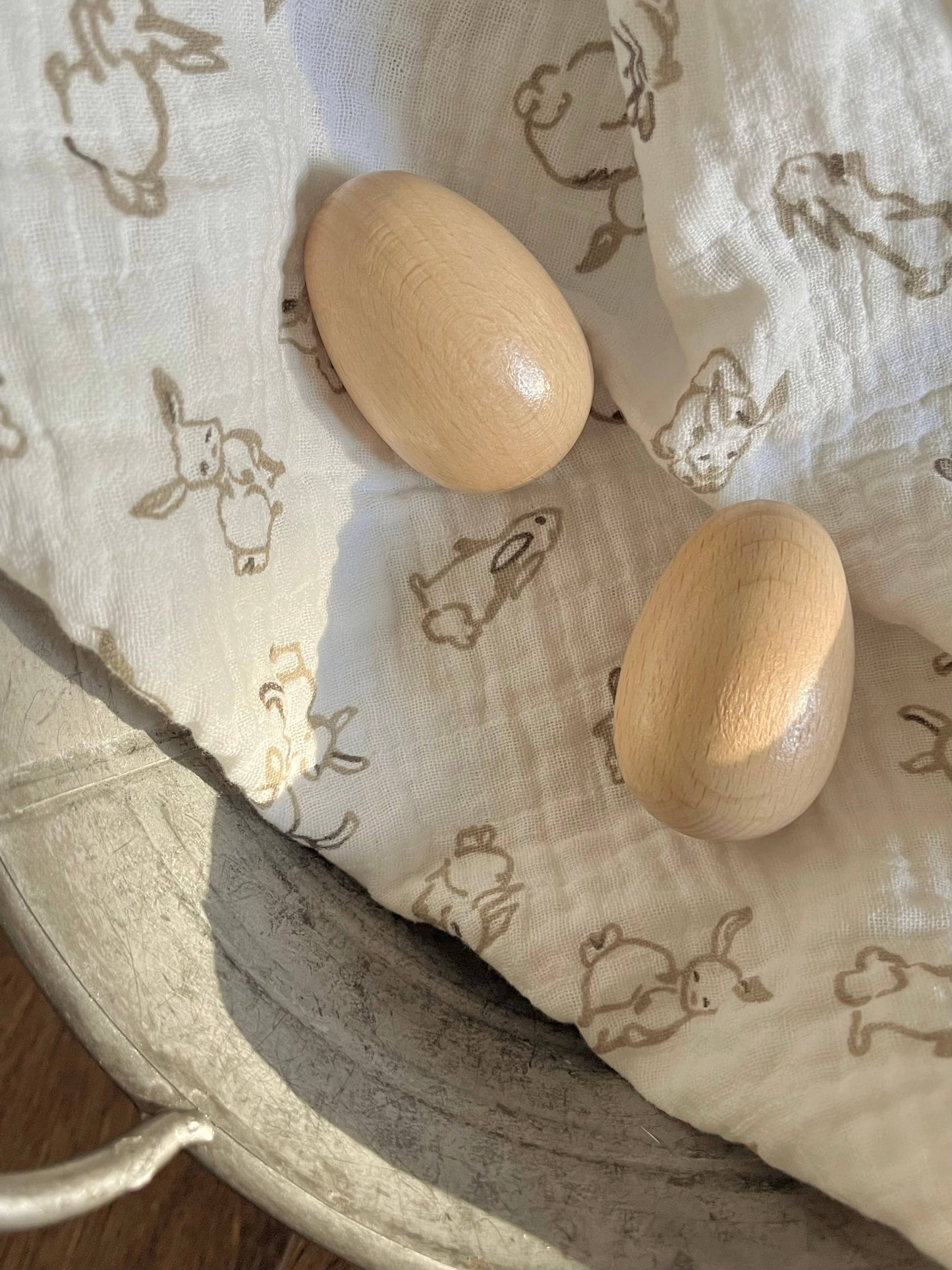 Two wooden egg shakers on a baby blanker with rabbit prints