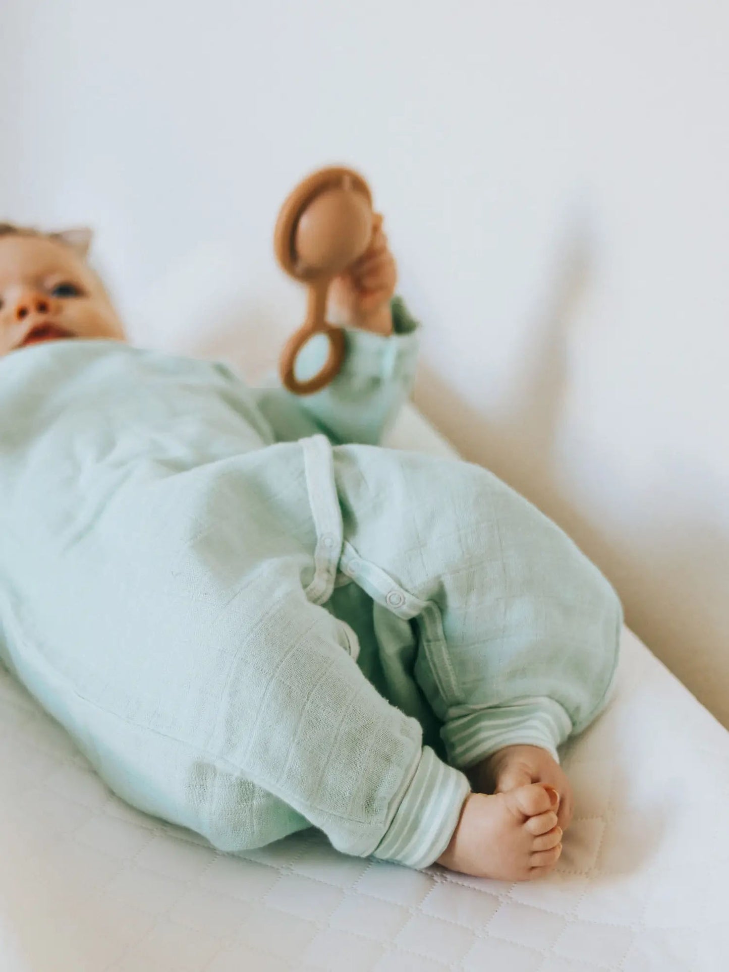 baby laying on a bed holding a rattle in the Muslin Side Snap Sea Wrap Kimono by under the nile
