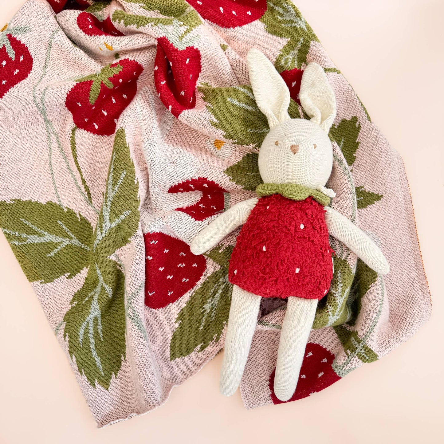 White plush bunny toy in a red dress on a strawberry-patterned blanket