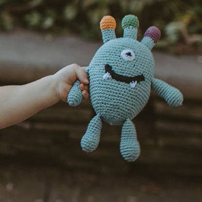 Hand holding a crocheted alien toy with colorful hair against a blurred natural background