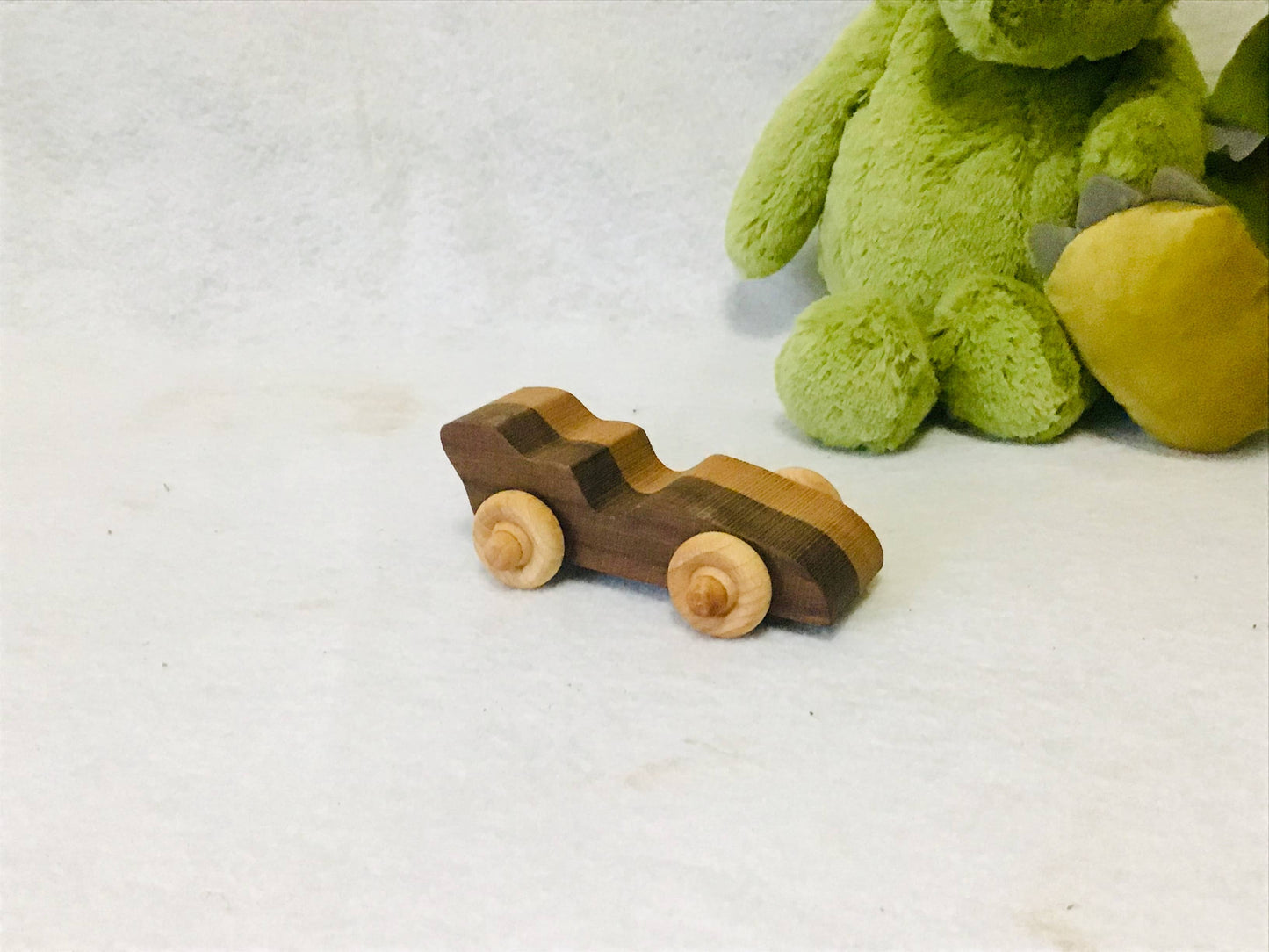 Wooden toy racecar next to a green plush toy on a white surface