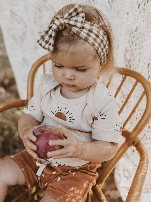 child sitting in a chair holding a pomegranate wearing sun organic short sleeve onesie