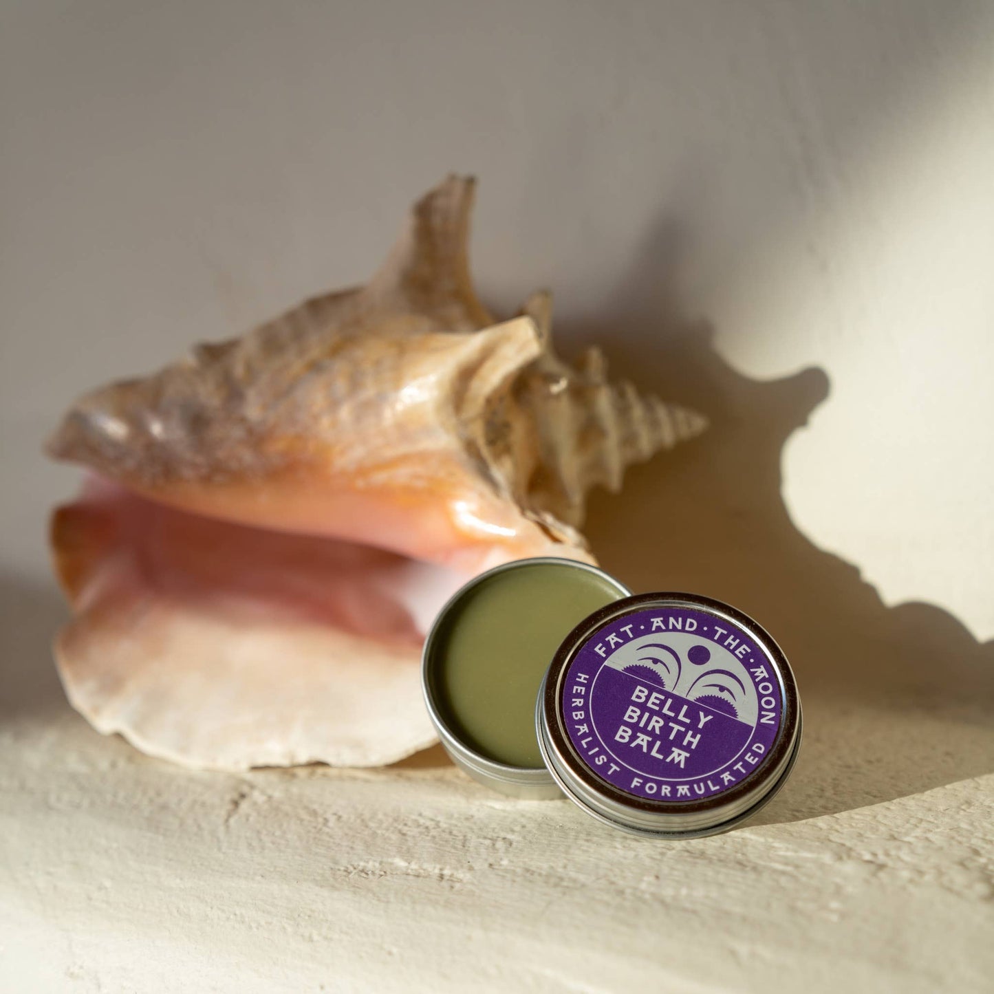 a tin of belly birth balm next to a seashell