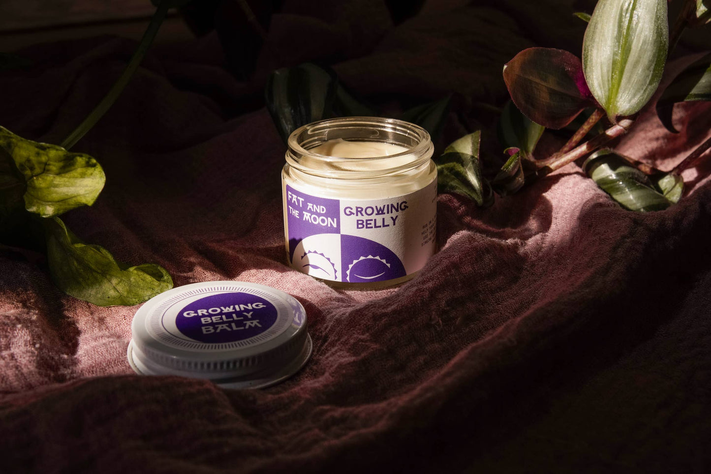 an open jar of grow belly balm on a cloth surrounded by plant cuts