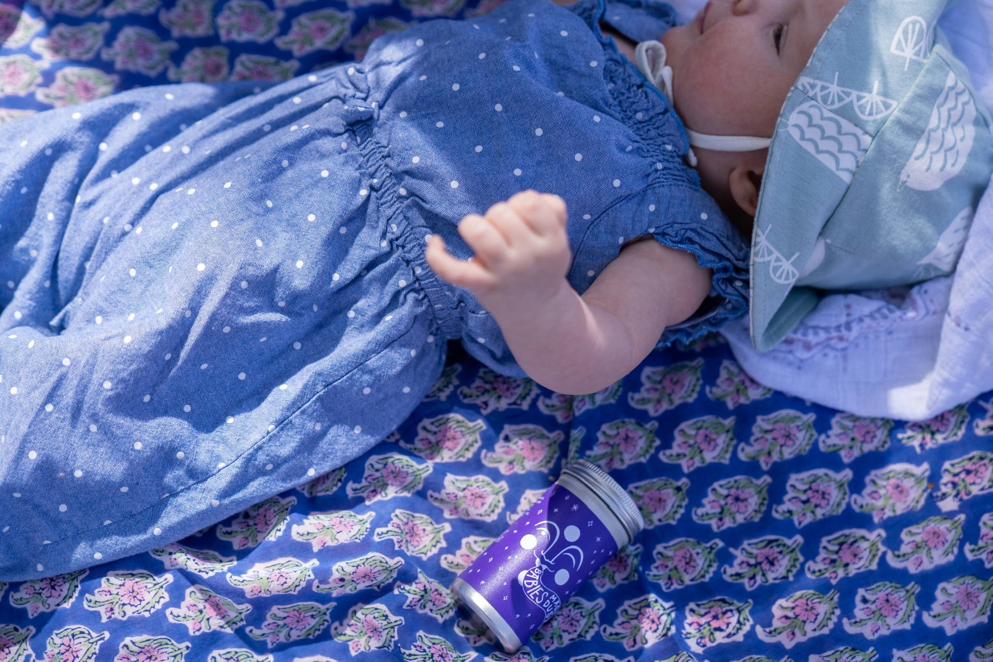 a baby wearing a summer outfit laying on a blanket outdoors next to a container of babies magic dust