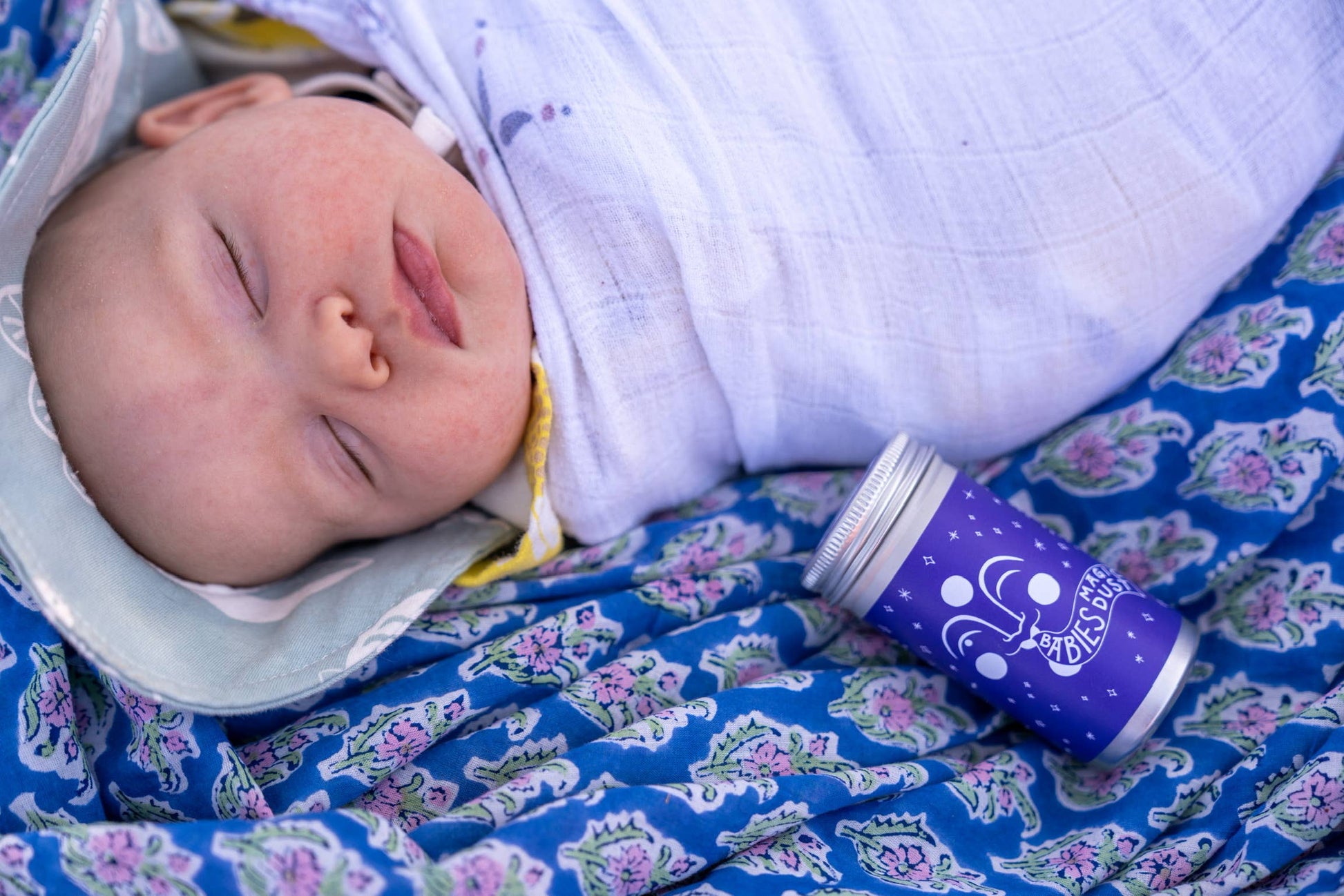 a baby swaddled and asleep next to a container of babies magic dust by Fat and the Moon