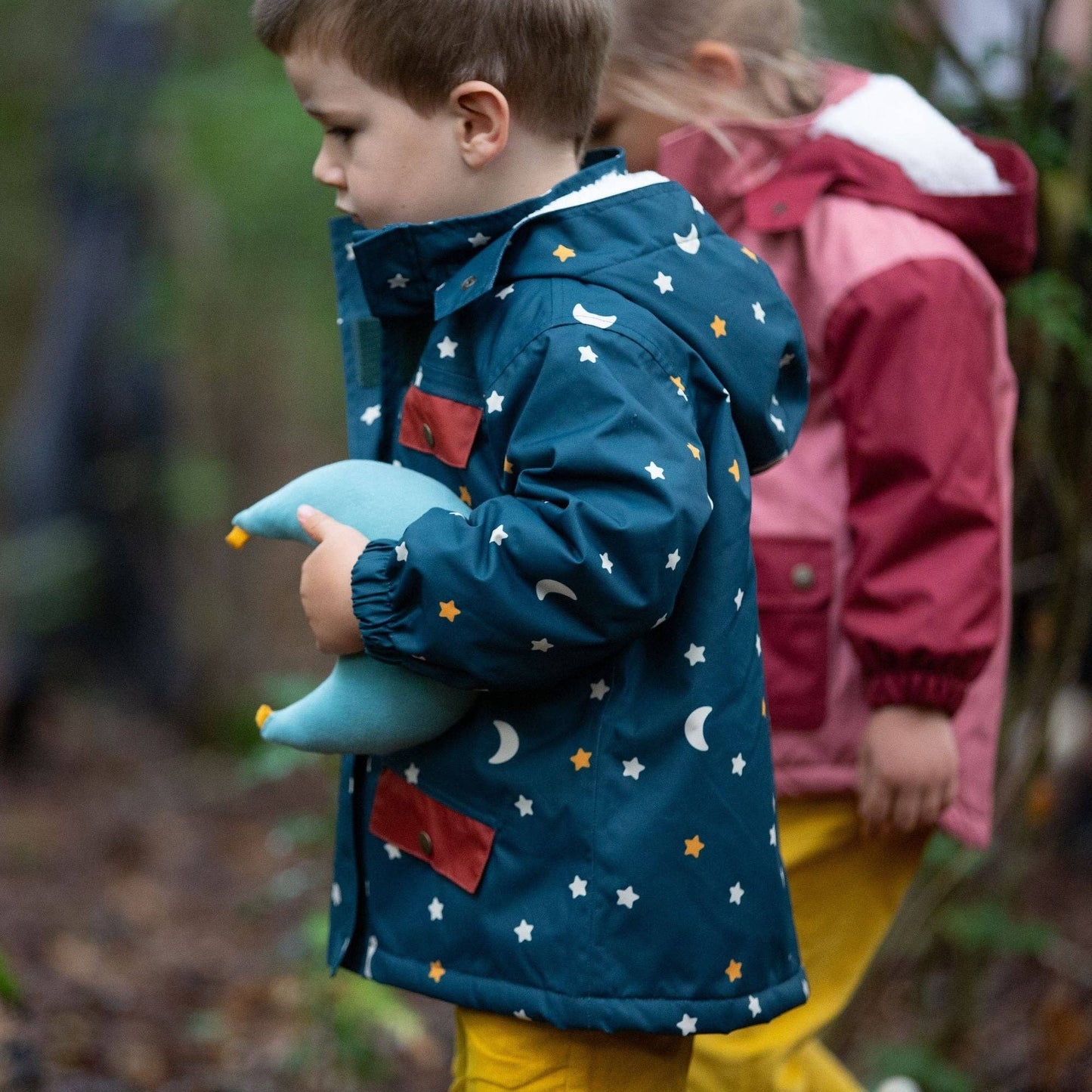 A child walking outdoors holding a soft moon toy and wearing a starry night recycled winter coat