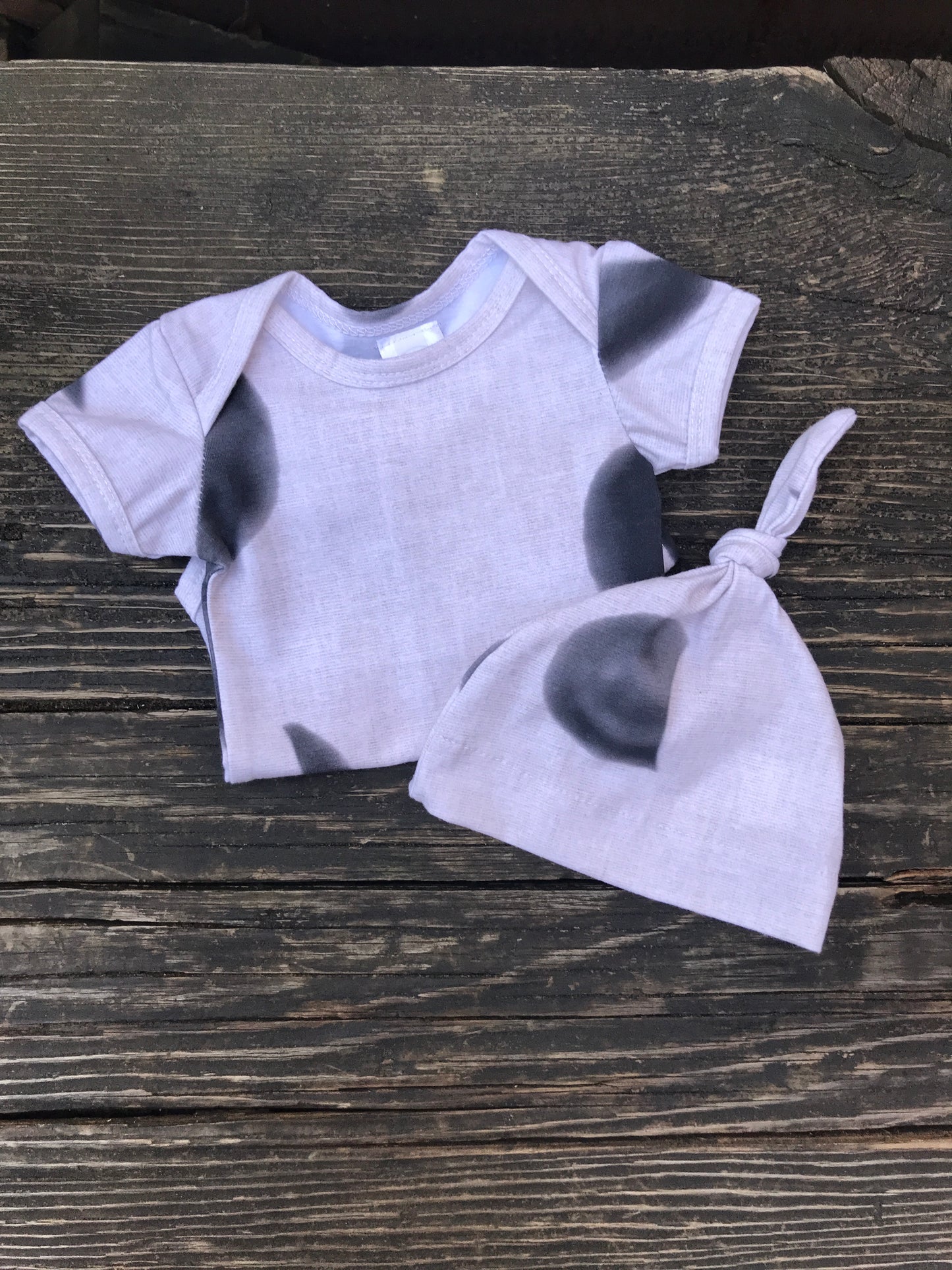 Short sleeve moon phase onesie with knot hat on a wood bench