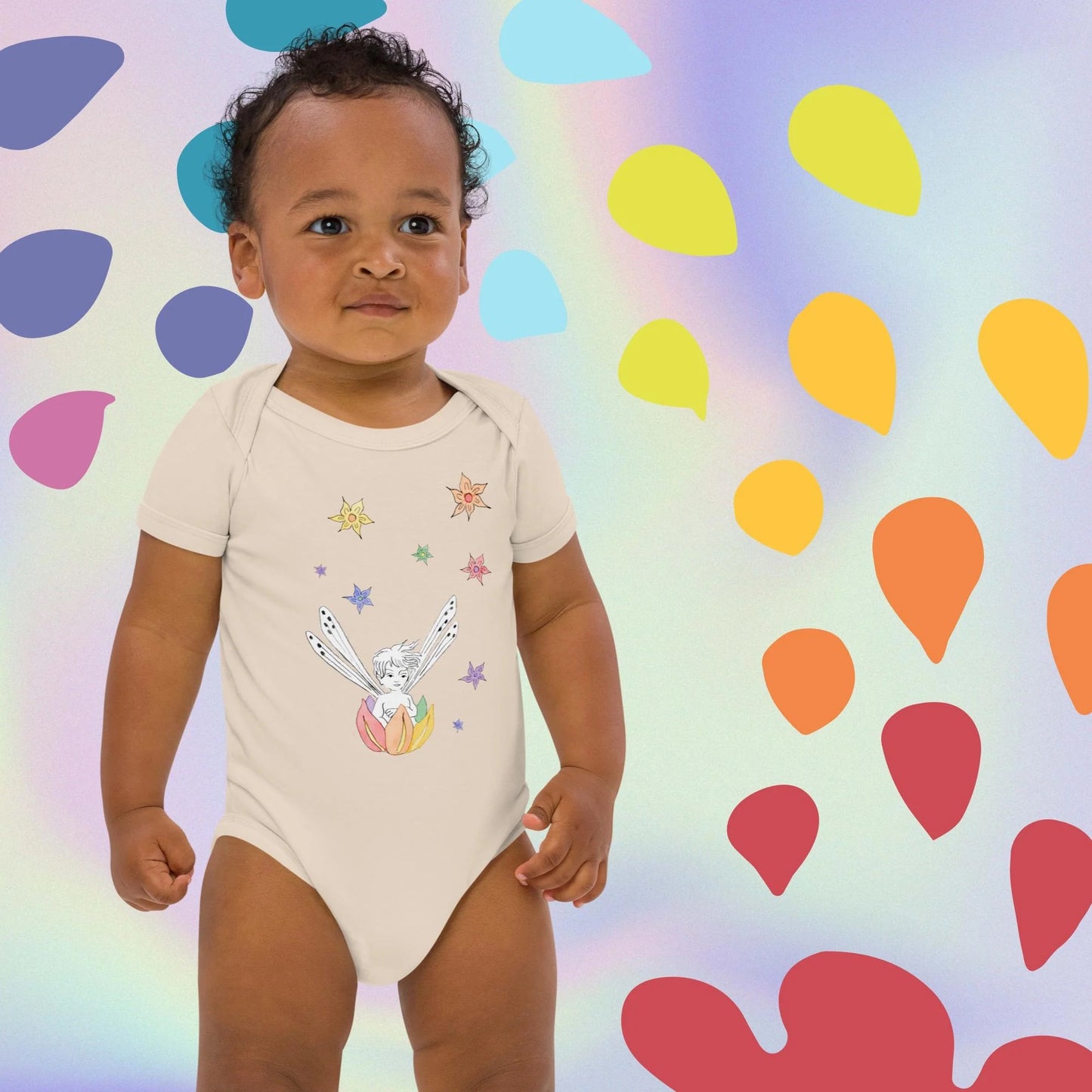 a baby standing in front of a colorful background wearing a rainbow fairy boat organic onesie