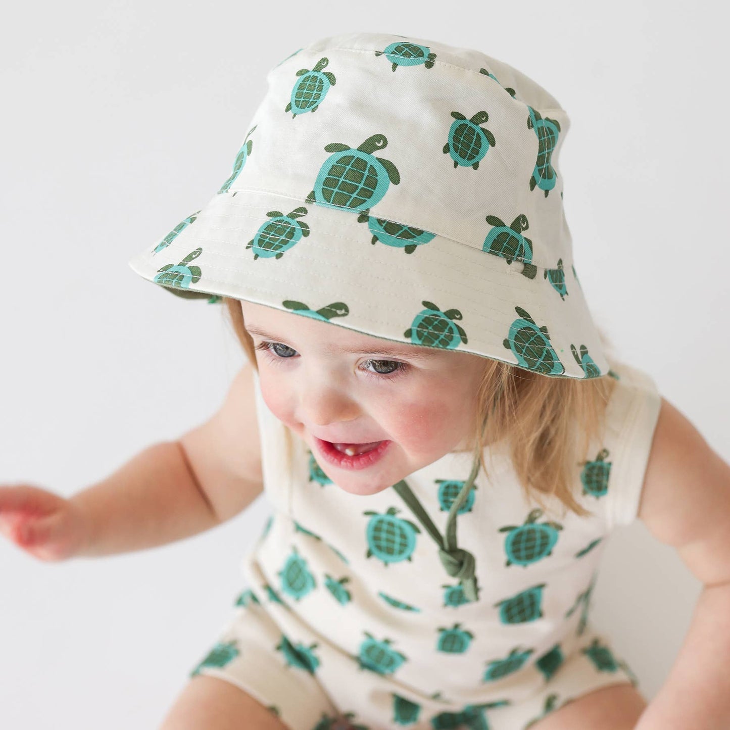 a baby wearing matching turtle romper and bucket hat
