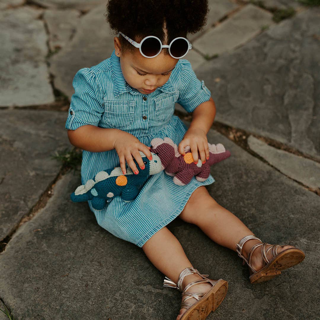 Child in a blue dress sitting on a stone path with dinosaur toys