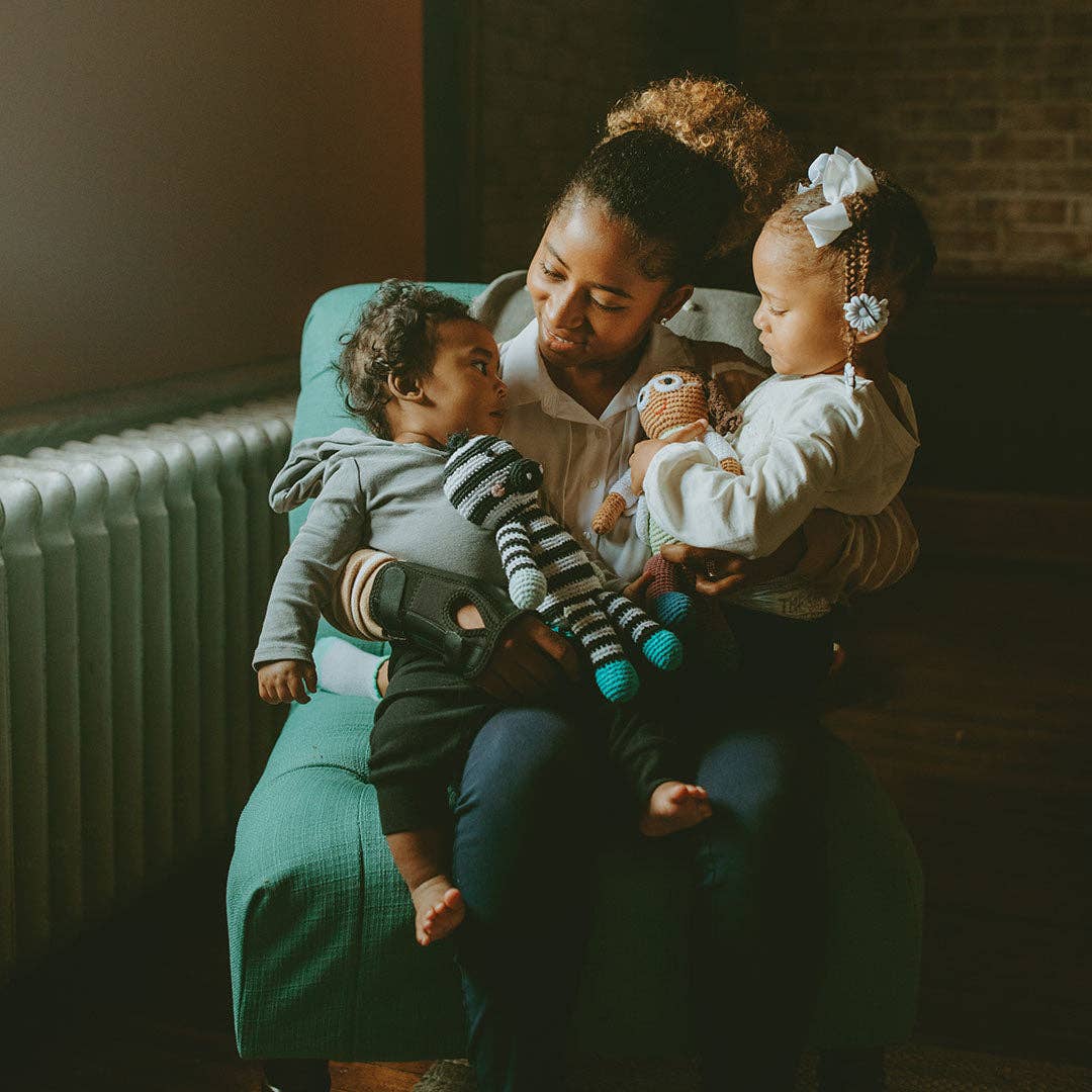 Person sitting on a green chair holding two children, both holding a knitted toy.