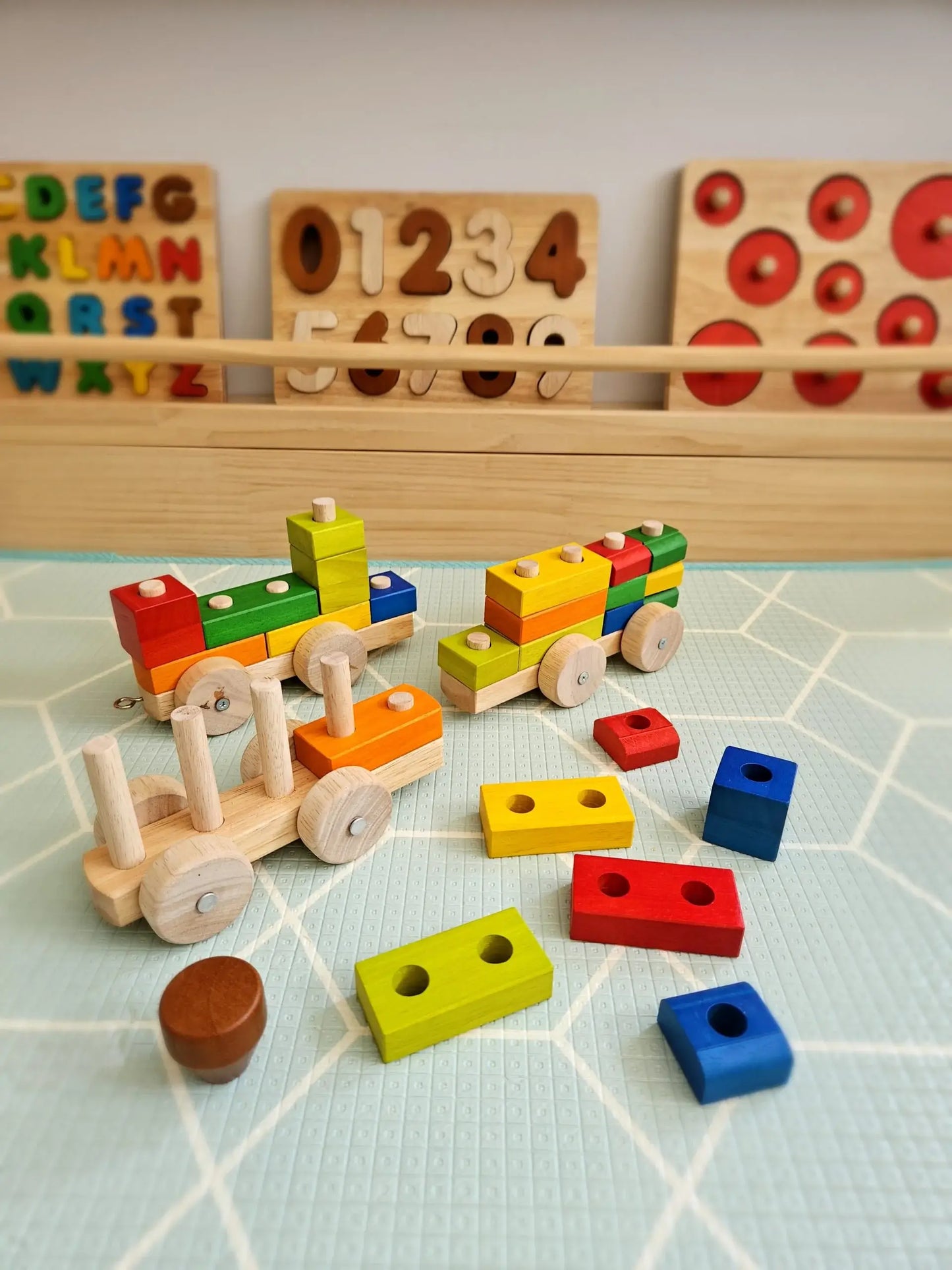 Colorful wooden toys including a train set and geometric shapes on a light blue grid floor