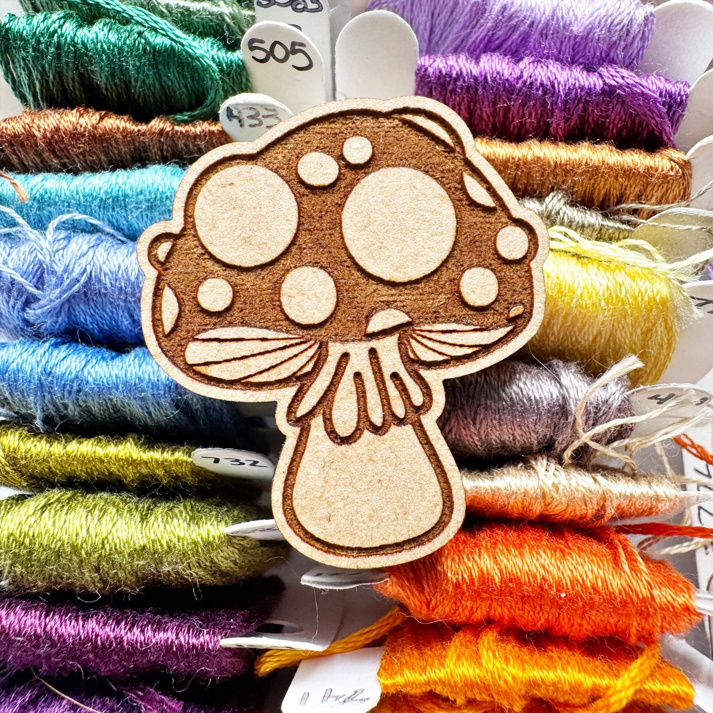 Wooden mushroom-shaped needle holder on a background of colorful thread.