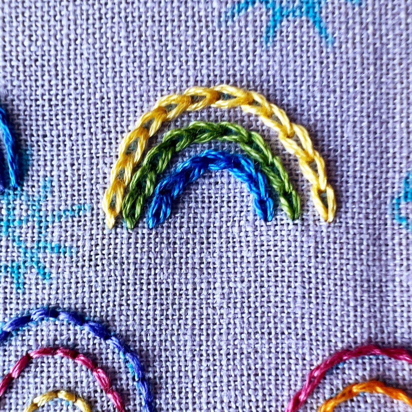 Embroidered rainbow design on fabric with multicolored threads.