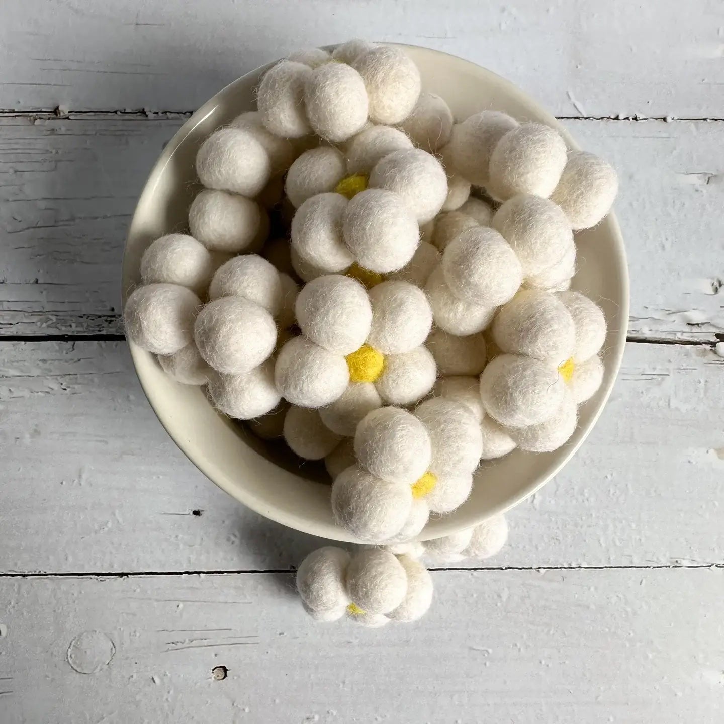 a bowl of white felt daisies on a wooden table