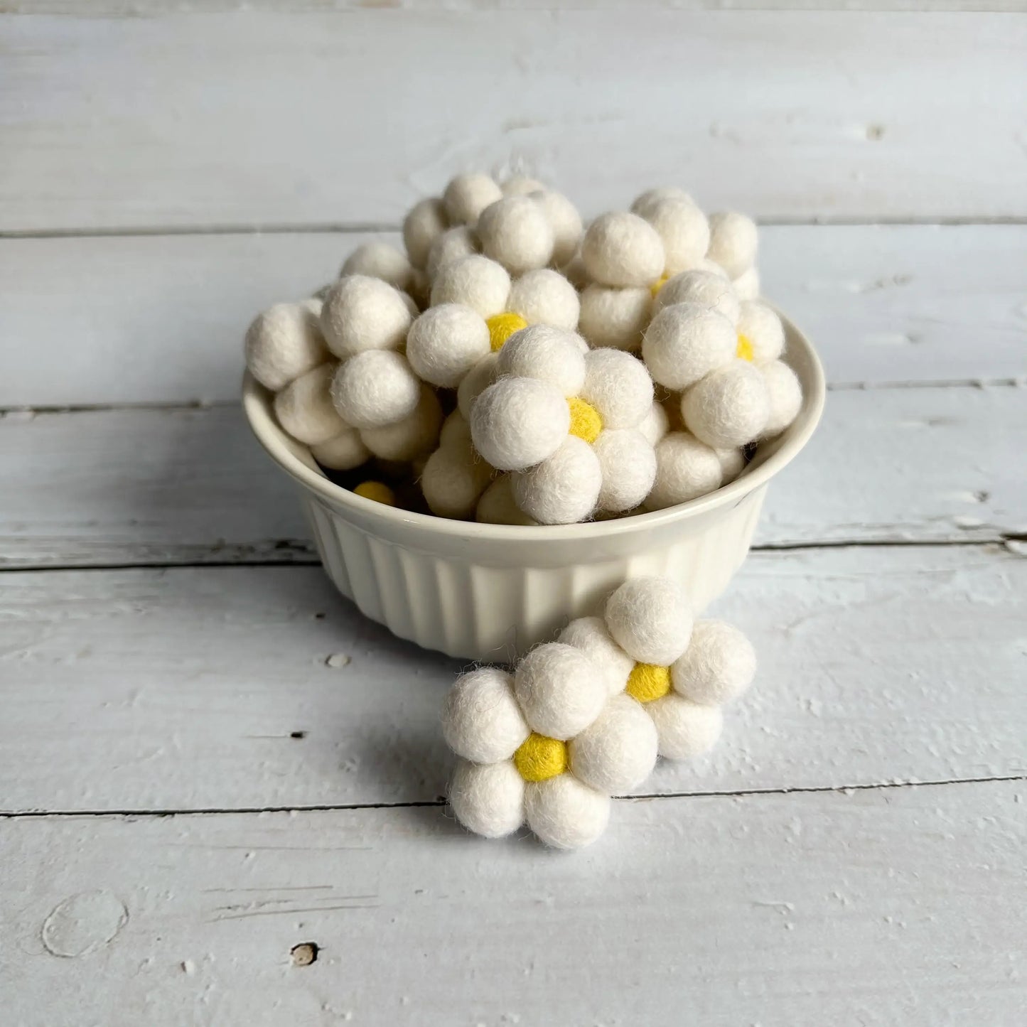 a ceramic bowl full of white felt daisies on a wooden table