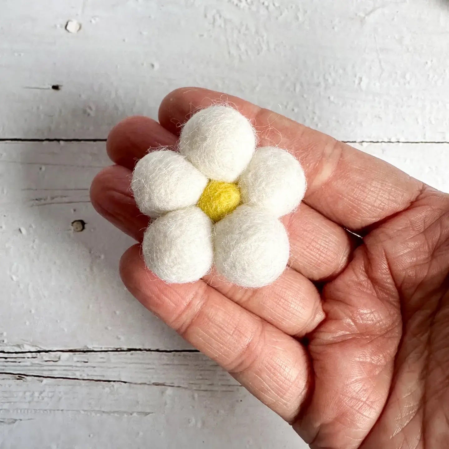 a hand holding a small felt daisy