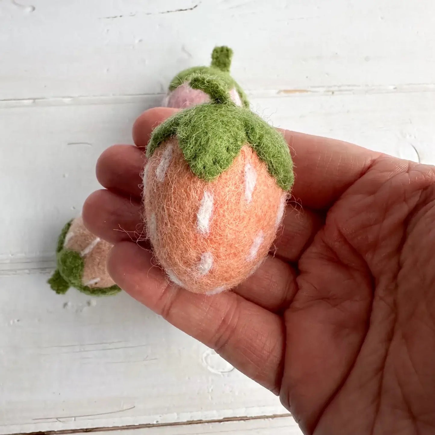 a hand holding a pink felt strawberry