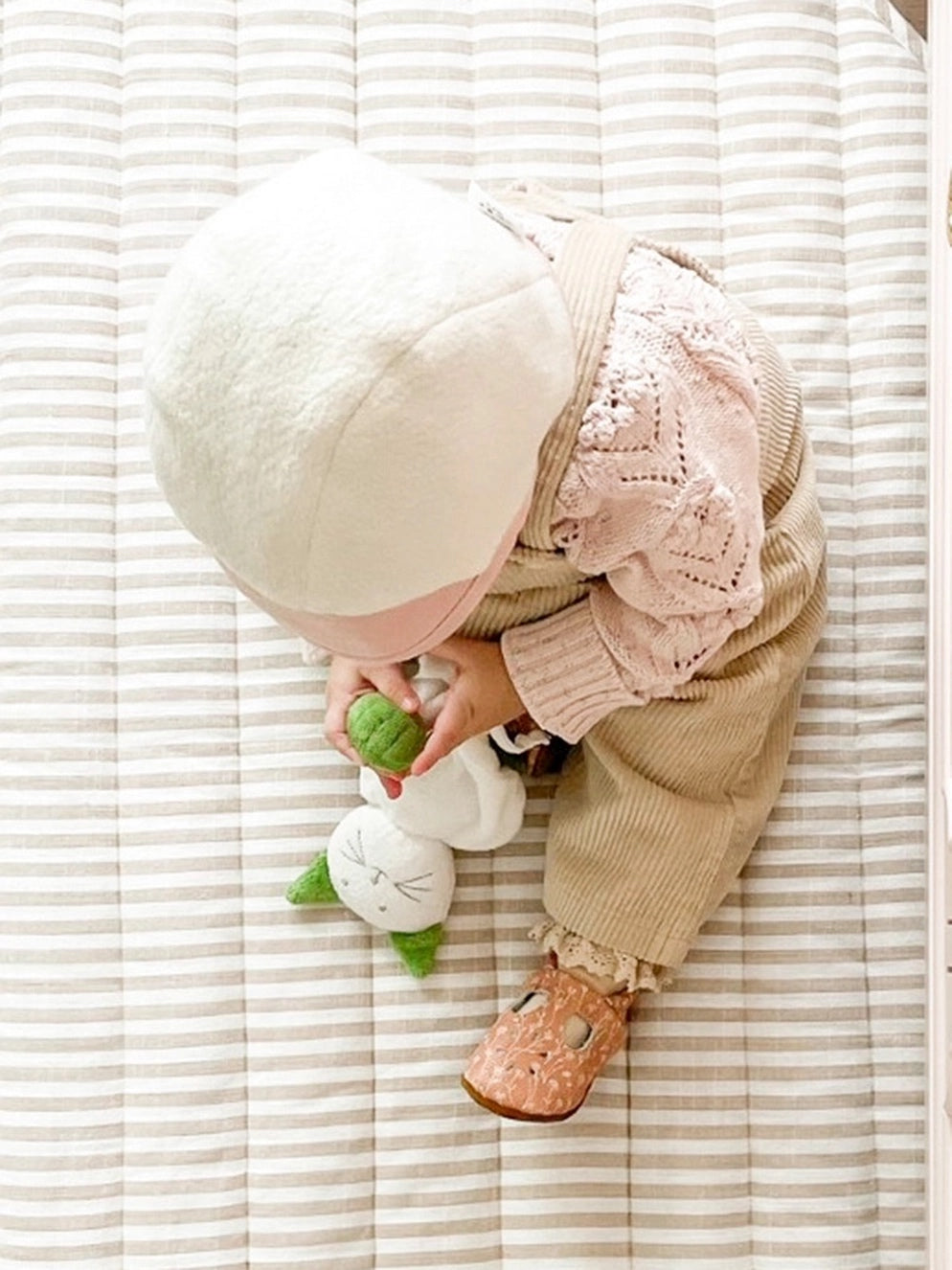 baby sitting on a bed playing with cece the cat baby toy