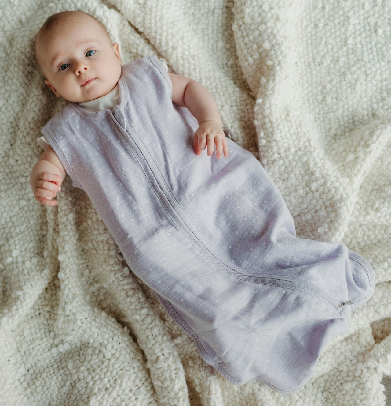 baby laying on a blanket wearing a lavender stars muslin sleep sack