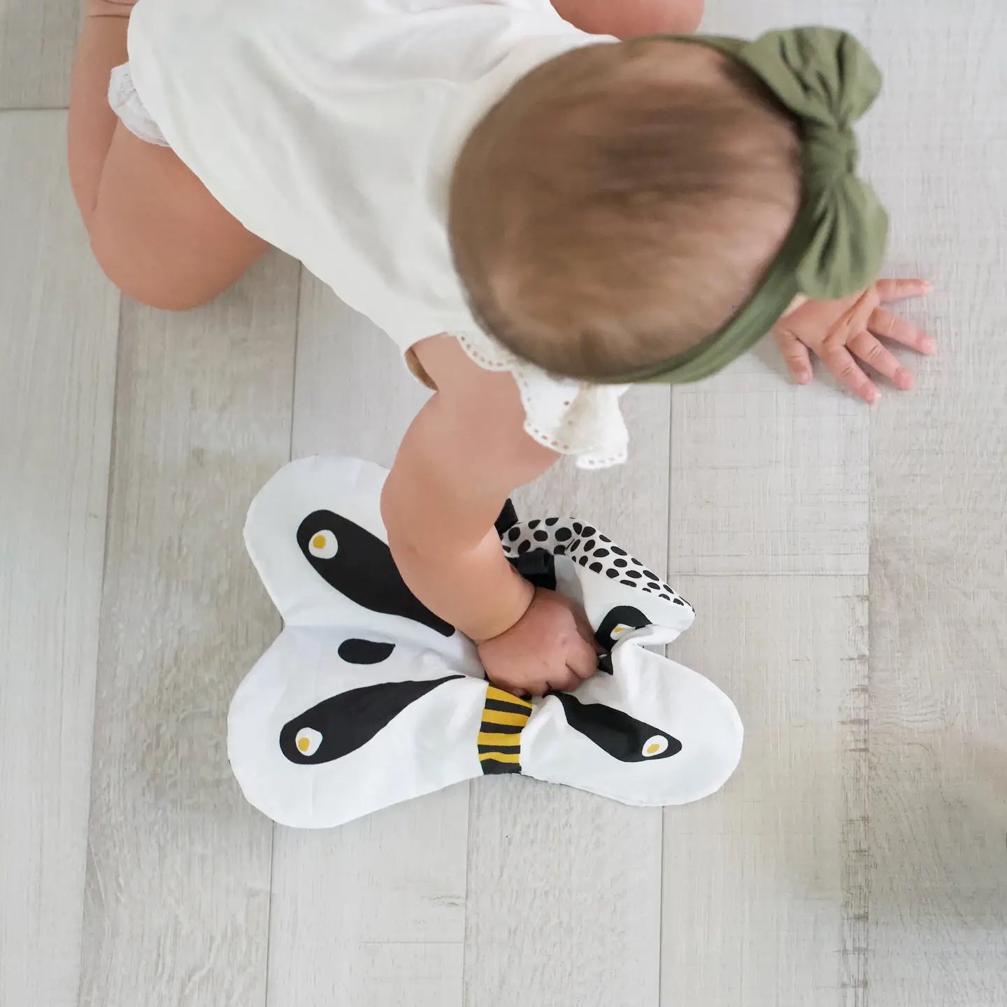 Baby playing with a butterfly crinkle toy on a wooden floor